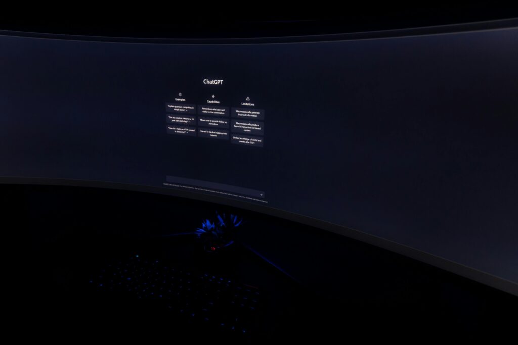 Close up of a dark room with a curved monitor showing the chatgpt interface on screen.